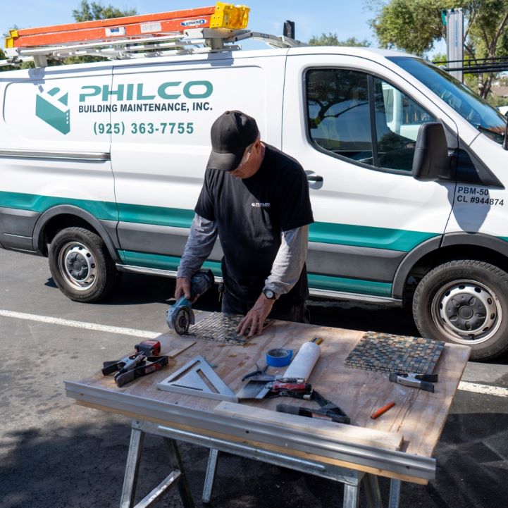 A Philco employee cutting tiles at a work bench with a Philco truck behind him